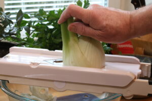 Image of fresh fennel being sliced on a mandoline for the tomato soup base. 