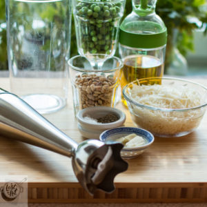 Prepped ingredients consisting of frozen peas, graded parmesan, toasted pine nuts, garlic, salt/pepper and olive oil.